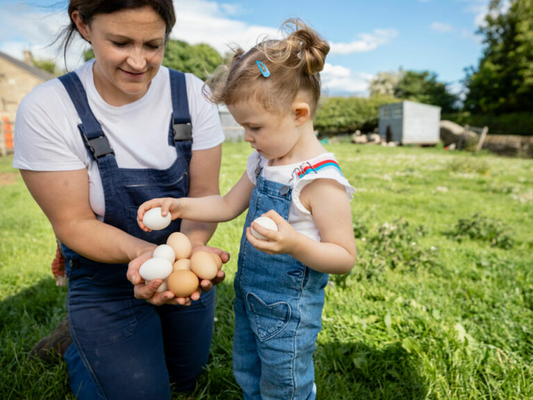 Familienhelferin auf einem landwirtschaftlichen Betrieb. Mit dem Kind der Familie sammelt sie die Eier von den Hühnern ein.