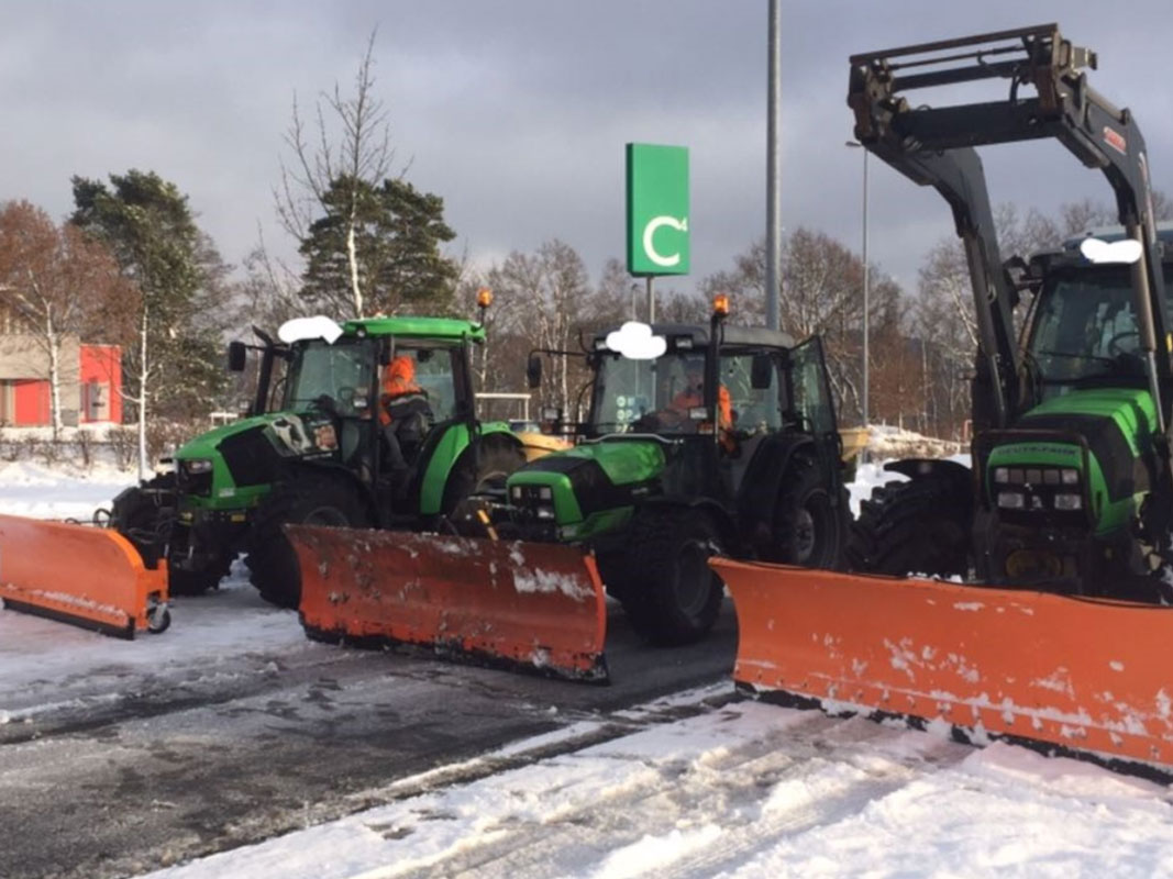 Auf dem Bild drei Traktoren mit Schneeschild auf einem Firmengelände beim Winterdienst zu sehen.