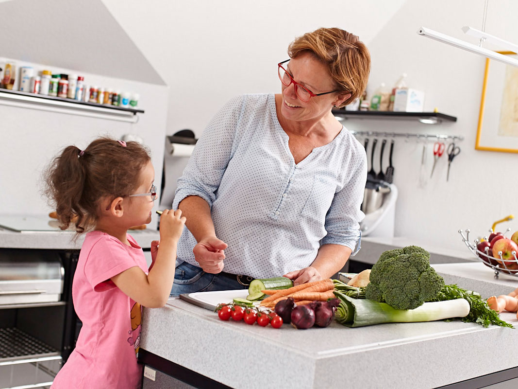 Eine Haushaltshilfe bereitet Essen mit einem Kind zu