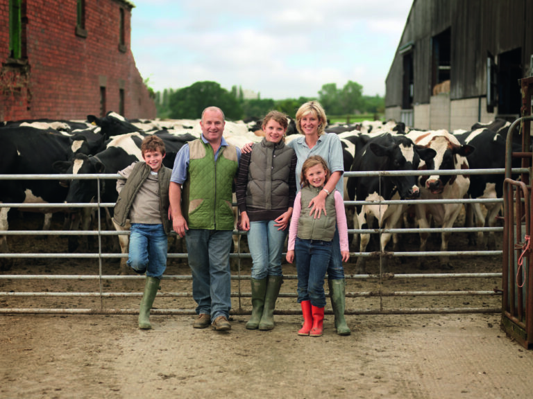 Vater, Mutter und ihre drei Kinder vor einer Herde schwarz-bunter Milchkühe